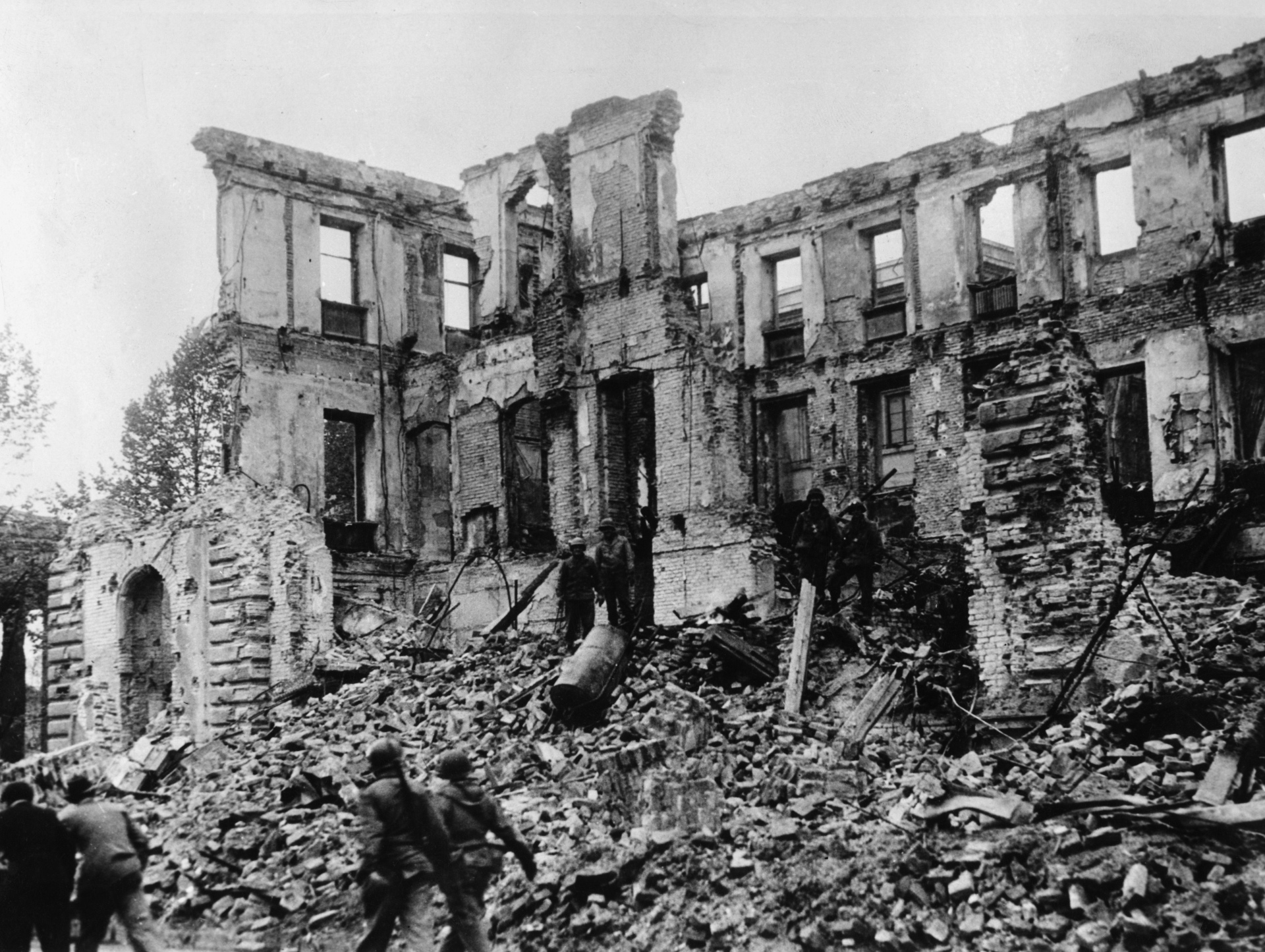 Bombed-out remains of the facade of a house with a pile of rubble lying in front of it.
