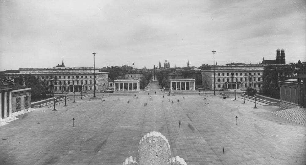 Schwarzweißaufnahme. Blick vom Dach der Propyläen auf den vollständig gepflasterten Königsplatz und die angrenzenden Parteibauten der NSDAP.