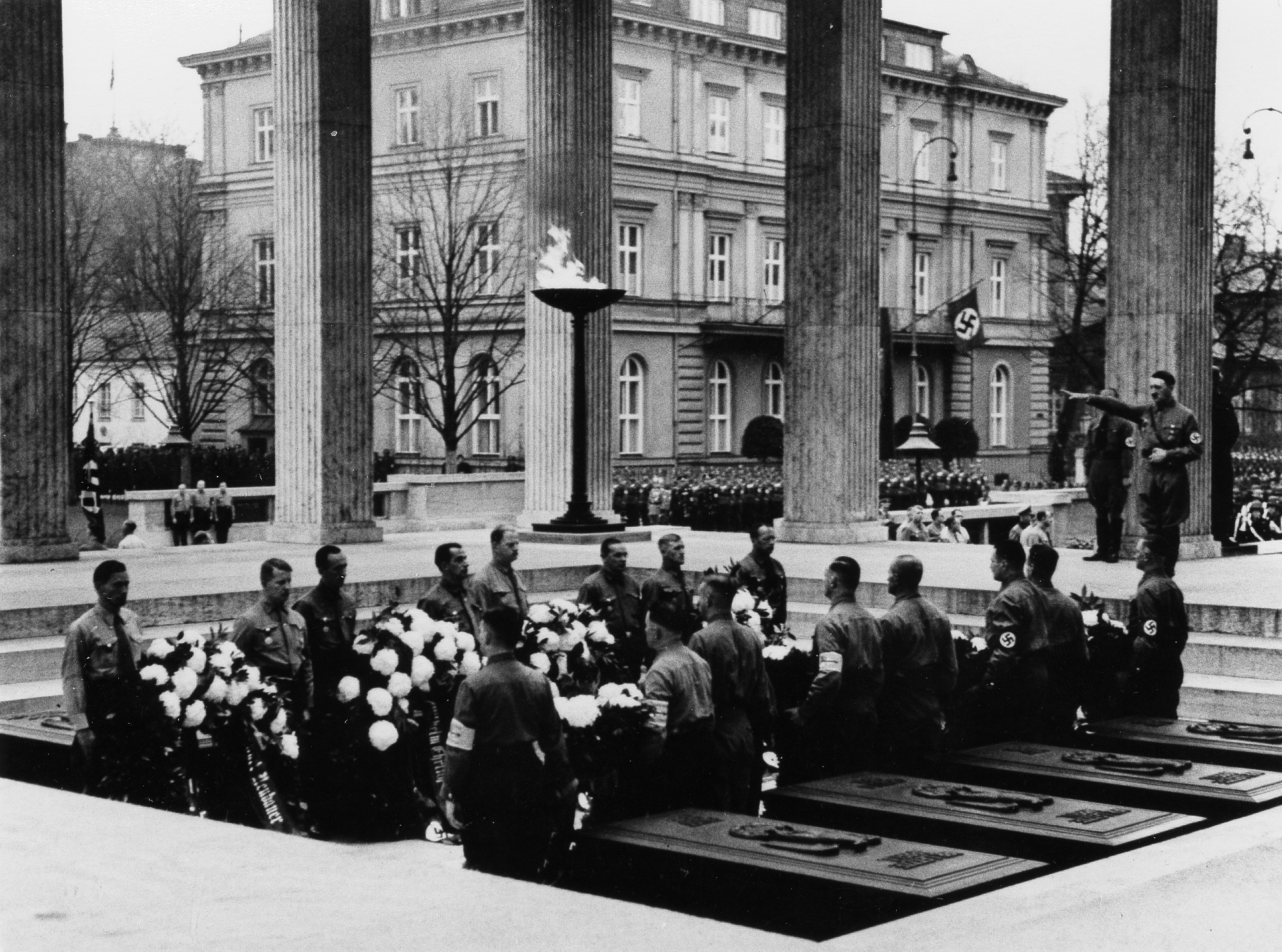 Adolf Hitler und einige SA-Männer bei der Beisetzung der Särge der Toten des 9. Nov. 1923 auf einem der ‚Ehrentempel‘. Im Hintergrund das ‚Braune Haus‘.