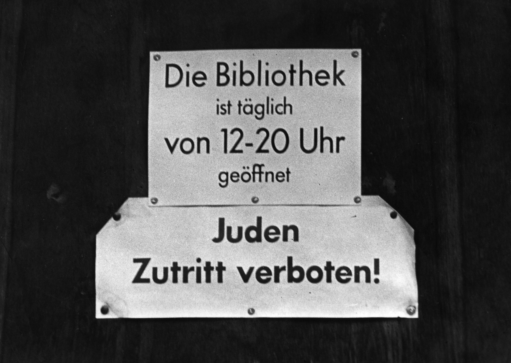 Schwarzweißaufnahme eines Schildes mit der Aufschrift „Die Bibliothek ist täglich von 12-20 Uhr geöffnet. Juden Zutritt verboten!“