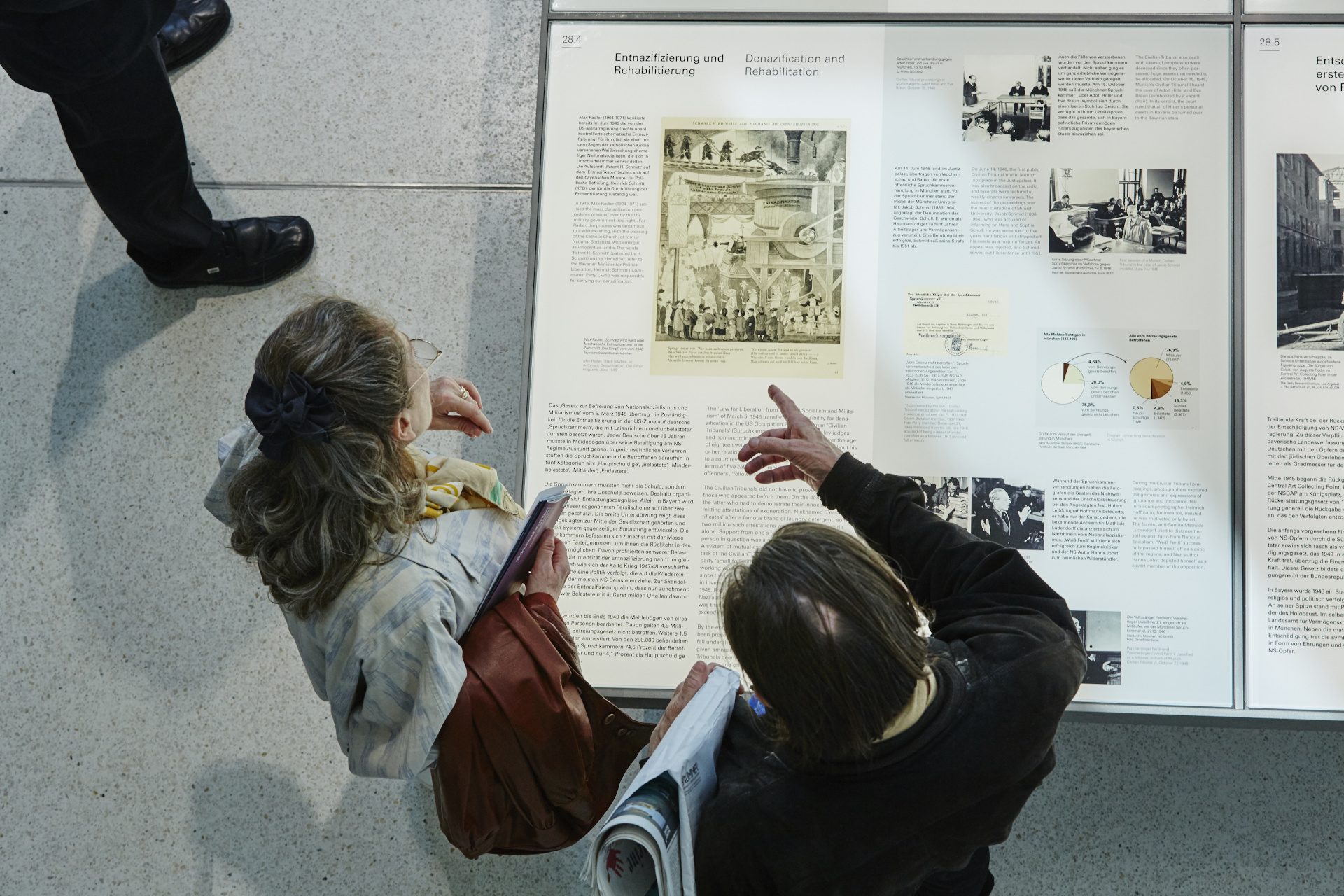 View from above of two people standing in front of an exhibition table with texts and images.
