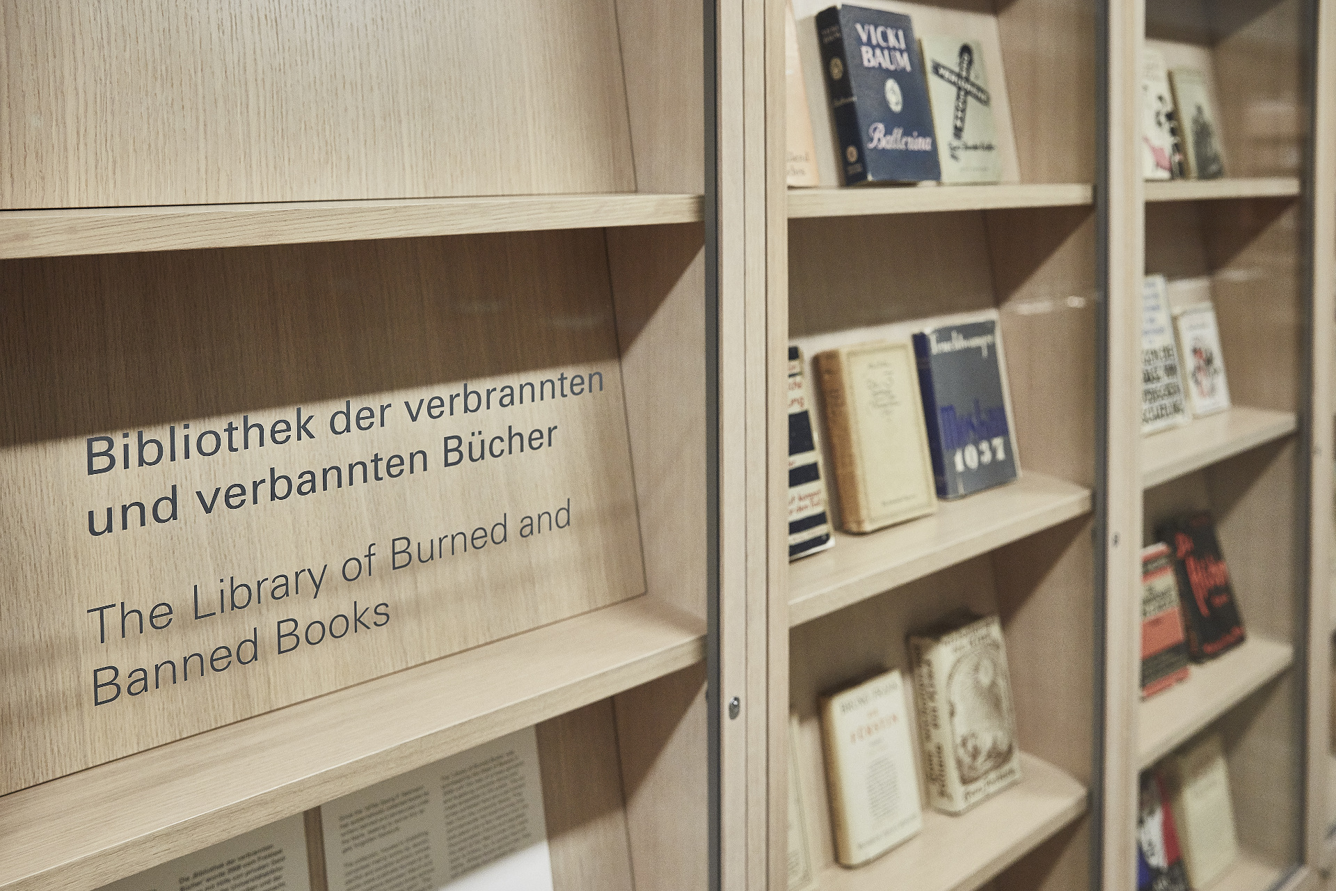 Auf einer Glaswand steht „Bibliothek der verbrannten und verbannten Bücher“. Daneben stehen Buchcover.