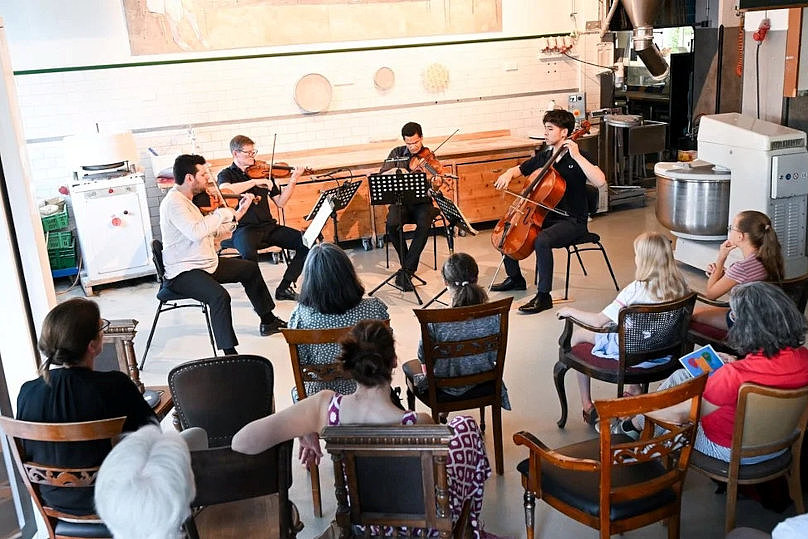 Vier Menschen mit Streichinstrumenten auf Stühlen spielen vor zehn sitzenden Menschen 