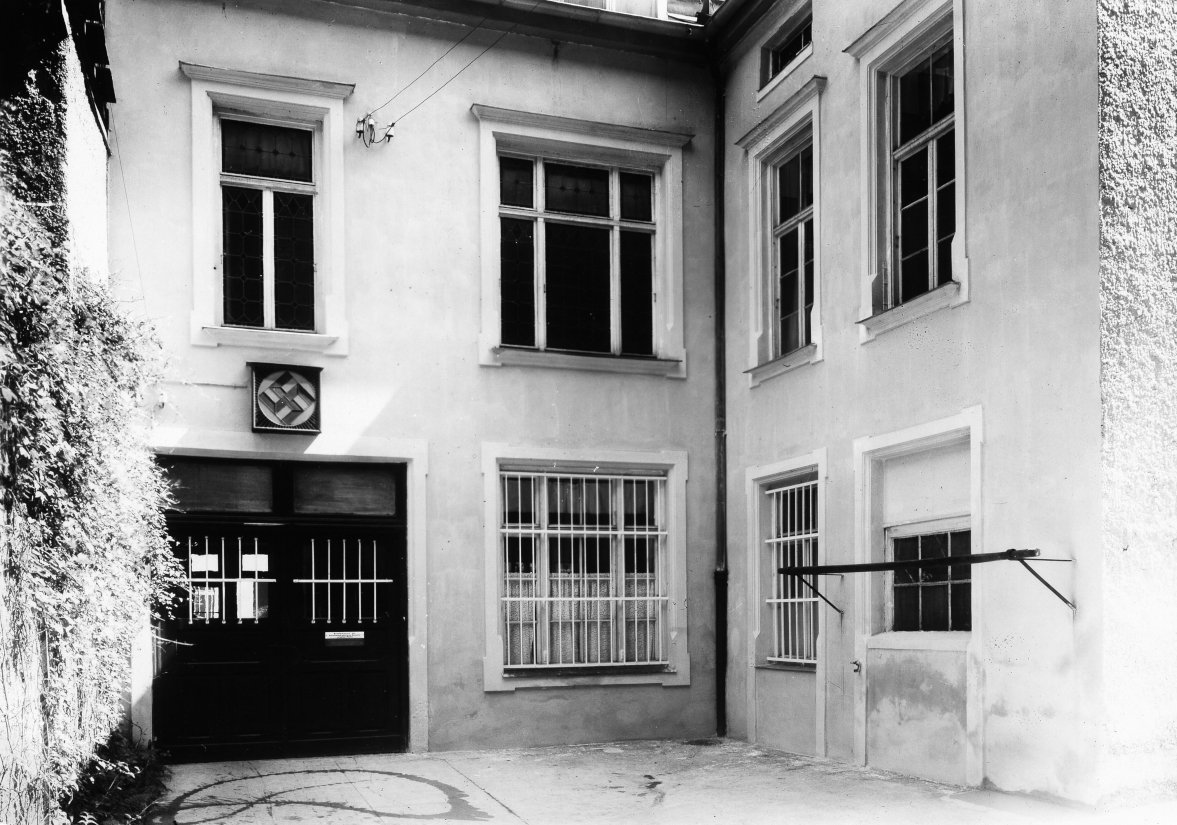 Facade of a corner building with several windows and a swastika above the entrance.