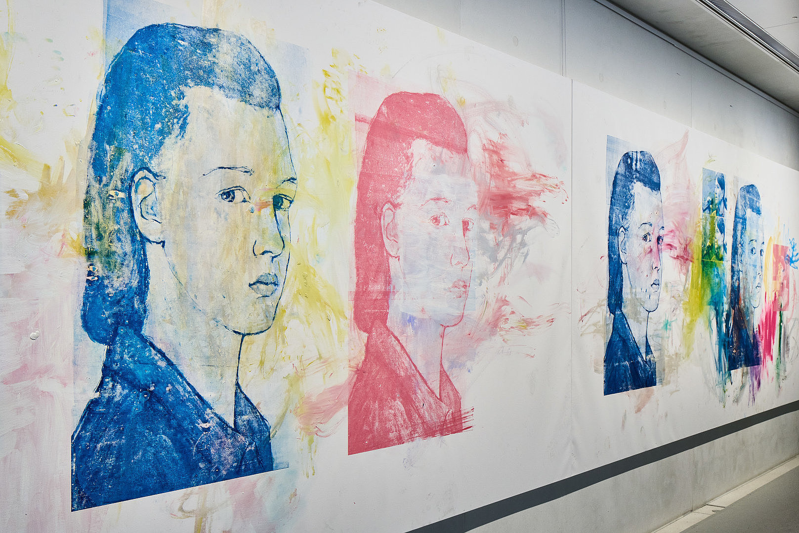 Gemälde mit fünf bunten Frauenköpfen an einer weißen Wand 