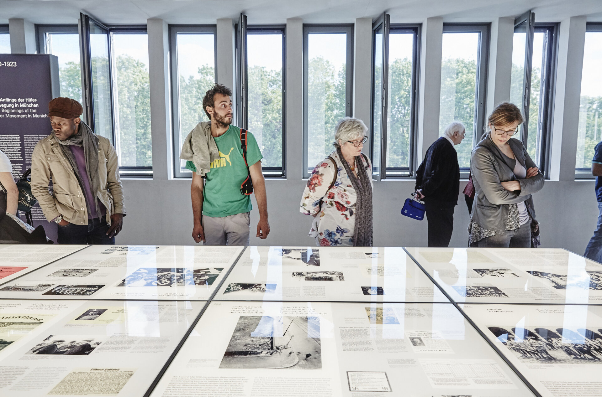 Personen blicken auf einen Tisch mit Ausstellungstexten, Bildern und Dokumenten. 